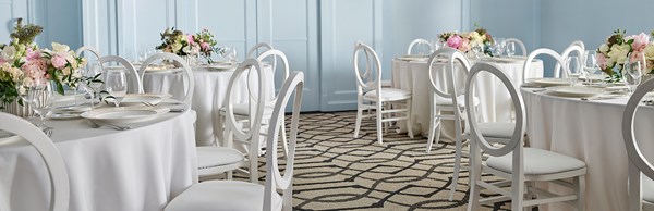 White chairs and round tables with flowers and dinner settings on them ready for a wedding