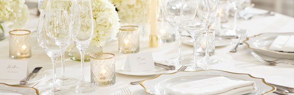 White dinner settings and flowers laid on a table at a wedding reception in the ballroom