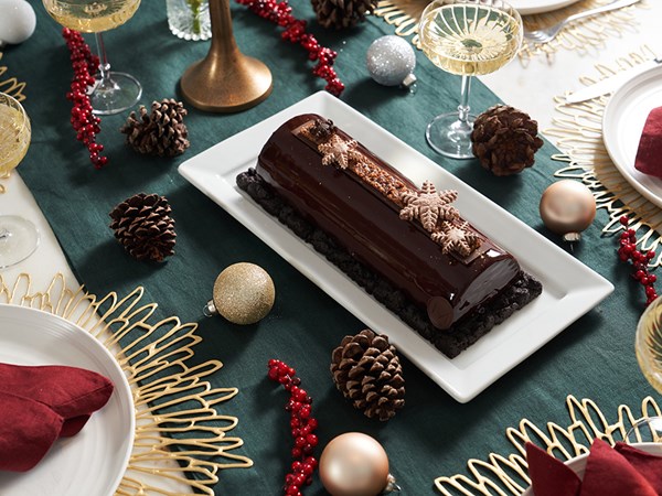 Festive holiday table setting with a buche de noel dessert centerpiece on a white platter and champagne coupe