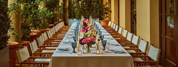 Long dining table on outdoor patio set for dining with colorful pink and red flowers down the middle