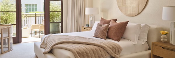 Bedroom with a brown fur throw and cushions on the bed, with balcony double doors open